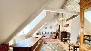 A loft-style room with a wooden dining table, benches, and a patterned rug. There is a sofa and a cabinet in the background. - Appartement de charme Cosy À 2 pas des plages (Larmor-Plage)