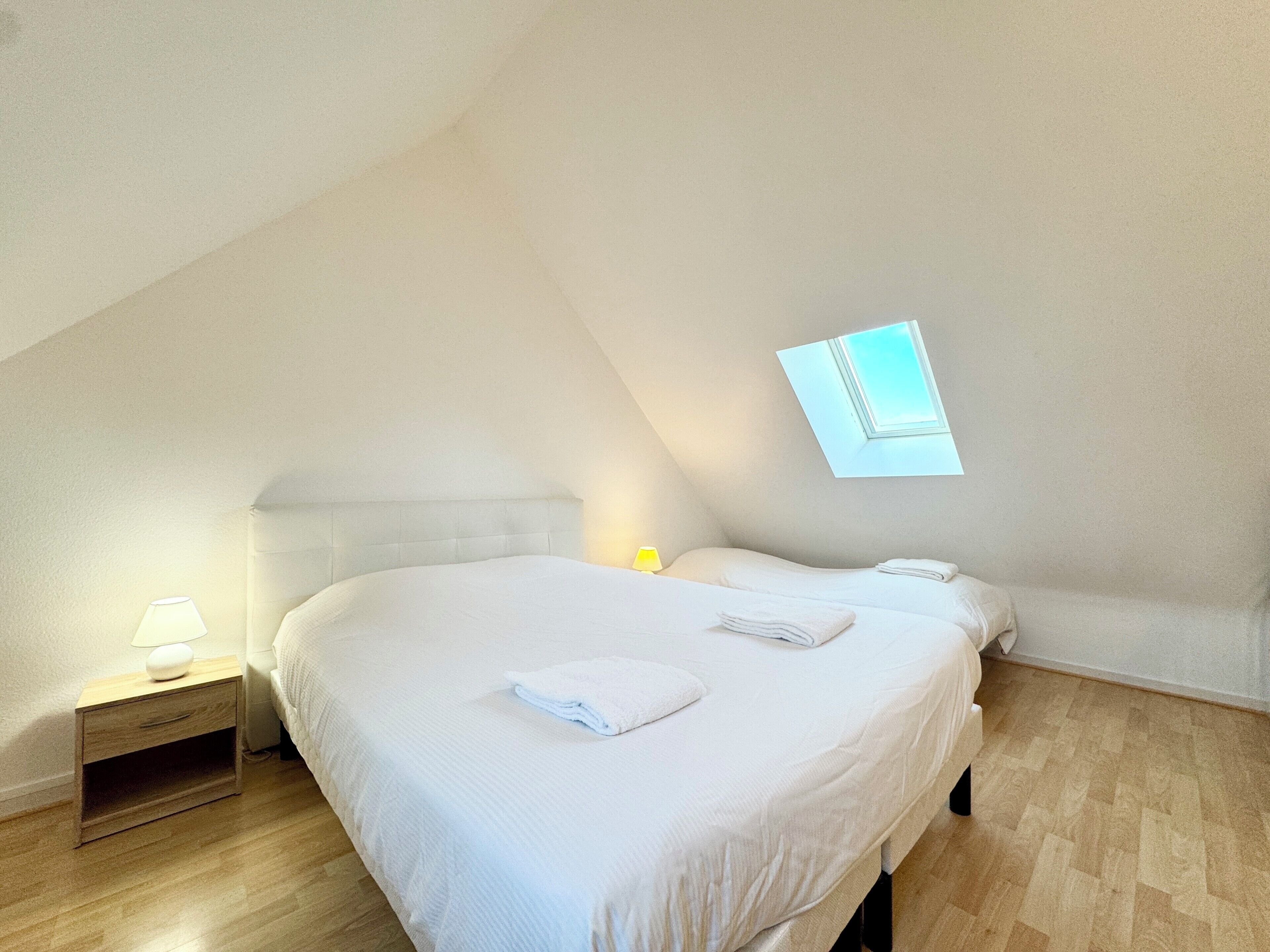 Une chambre à coucher avec un grand lit, une table de chevet, une lampe et une lucarne.