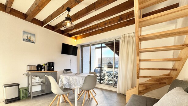 Um quarto aconchegante com uma mesa de jantar, cadeiras, um sofá, uma TV e uma varanda com vista.
