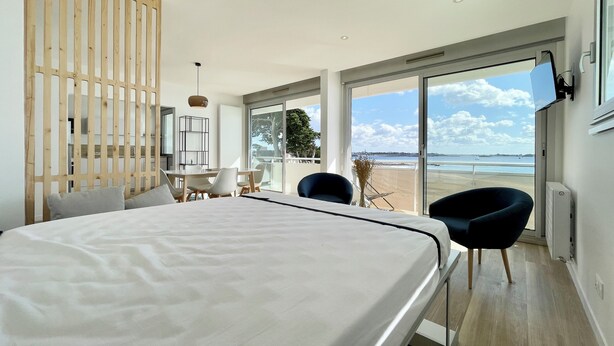 Ein modernes Hotelzimmer mit einem großen Bett, einem Essbereich und einem Balkon mit Blick auf den Strand.