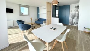 Ein modernes Wohnzimmer mit einem weißen Esstisch, blauen Sofas und einem großen Fenster.
