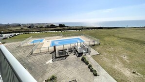 Ein Poolbereich mit zwei Pools, umgeben von einer eingezäunten Terrasse und einer Rasenfläche.
