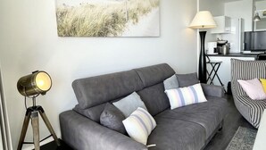 Ein modernes Wohnzimmer mit einem grauen Sofa, einer Stehlampe und einer Küche im Hintergrund.
