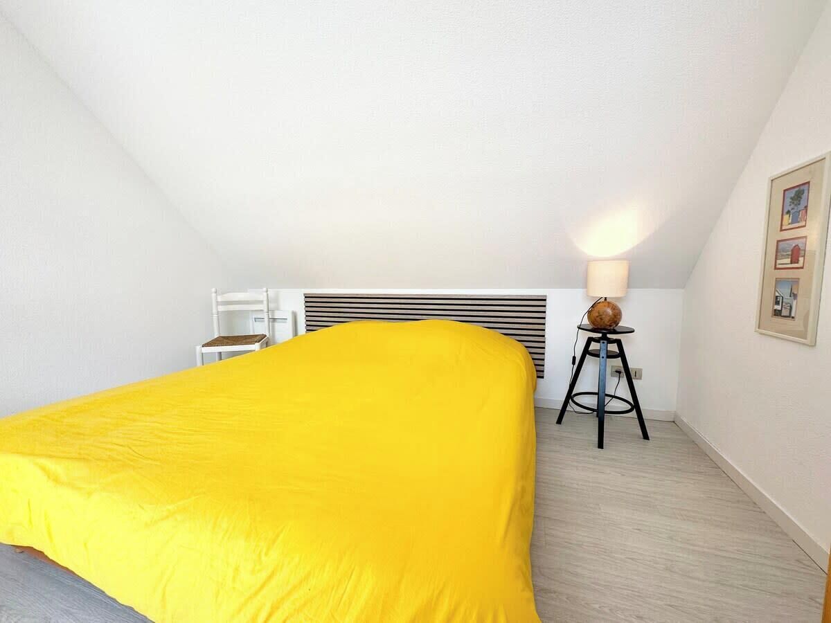 A bedroom with a bed covered in yellow bedding, a standing heater, and a small table with a lamp.