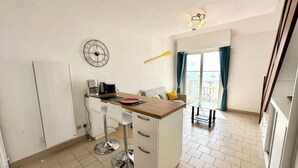 Une cuisine compacte dotée d’un îlot central, de meubles blancs et d’un coin repas avec une table et des chaises.