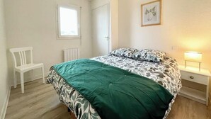 Une chambre à coucher comprenant un lit, une chaise, une table de chevet avec une lampe, une fenêtre et une porte.