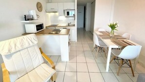 Une cuisine moderne avec des meubles blancs, un coin repas comprenant une table et des chaises, et un luminaire suspendu jaune.