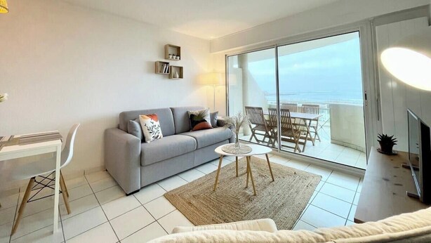 Un salon moderne avec un canapé gris, une petite table ronde et un balcon avec vue.