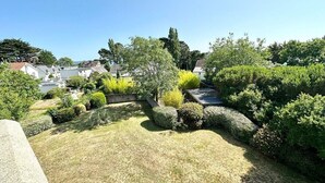 A landscaped garden with various shrubs and trees, a clear sky, and residential buildings in the background.