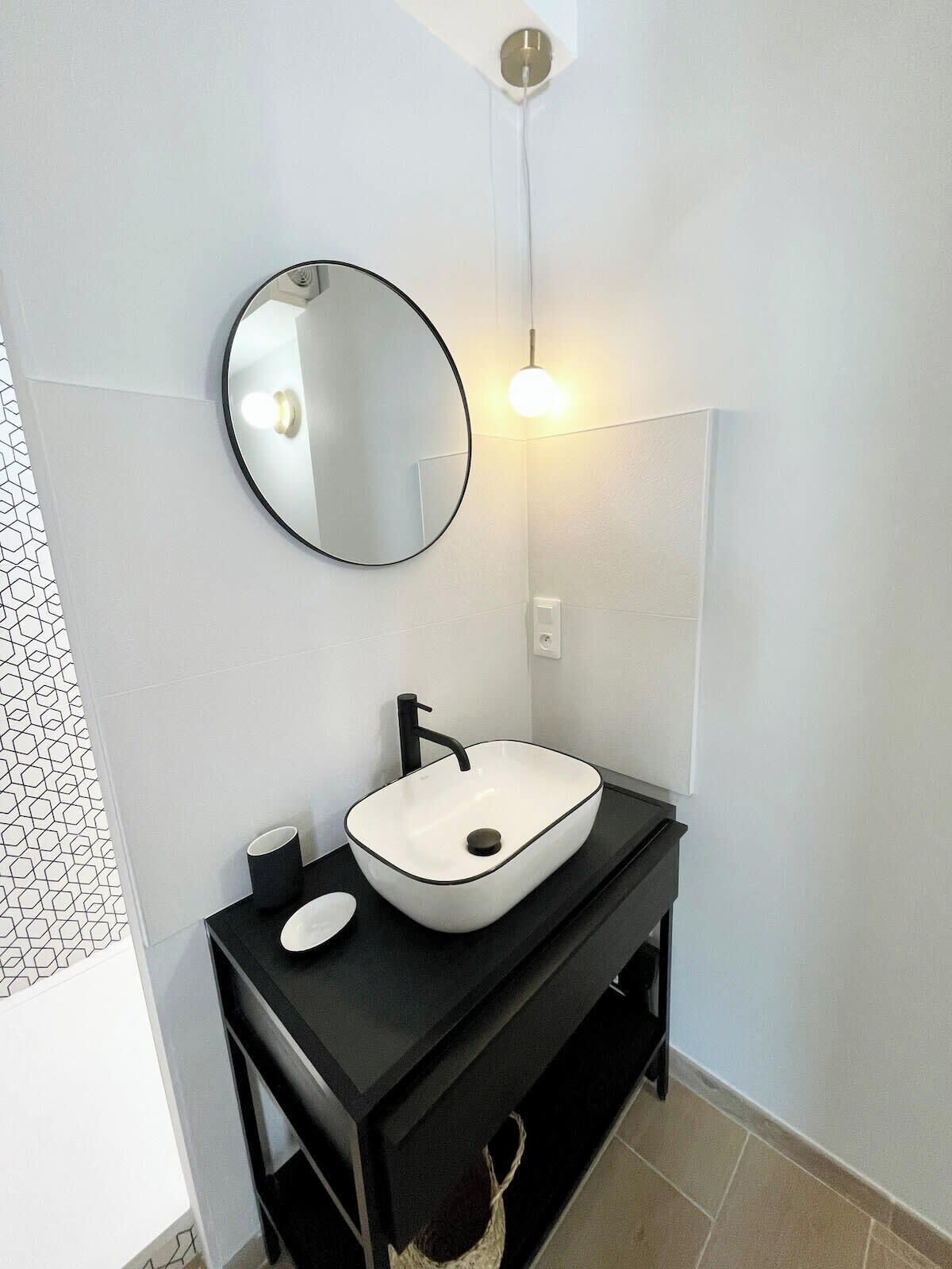 A modern bathroom with a round mirror, a white sink, and a black countertop.
