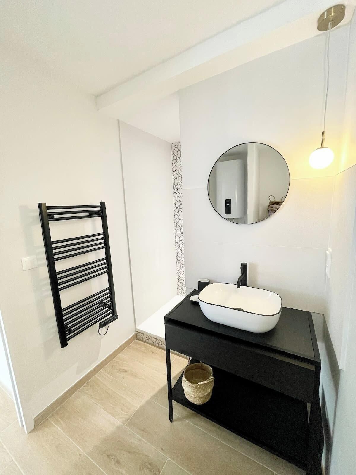 A modern bathroom with a black towel rack, a round mirror, and a white sink on a black countertop.