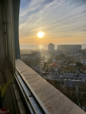 A cityscape with a sunset over the ocean, buildings, and a road with vehicles. - Impeccable 2-bed Apartment in Costa da Caparica (Almada)