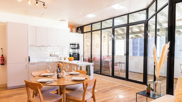 A modern kitchen with white cabinets, a dining table set for four, and a large sliding glass door leading to a balcony.
