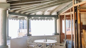 A covered outdoor seating area with a wooden floor, white chairs, and a round table.