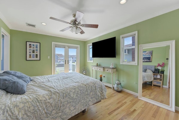 A bedroom with a bed, a ceiling fan, a dresser, and a TV mounted on the wall.