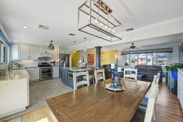 A spacious kitchen with a central island, a dining area with a wooden table, and a living room with a sofa and a large window. - Waterfront Escape in Long Island NY (massapequa)