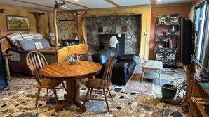A living room with a stone fireplace, a black leather sofa, a wooden dining table with chairs, and a patterned rug. - Magic Forest Farm's Mountain View Suite (Coeymans Hollow)