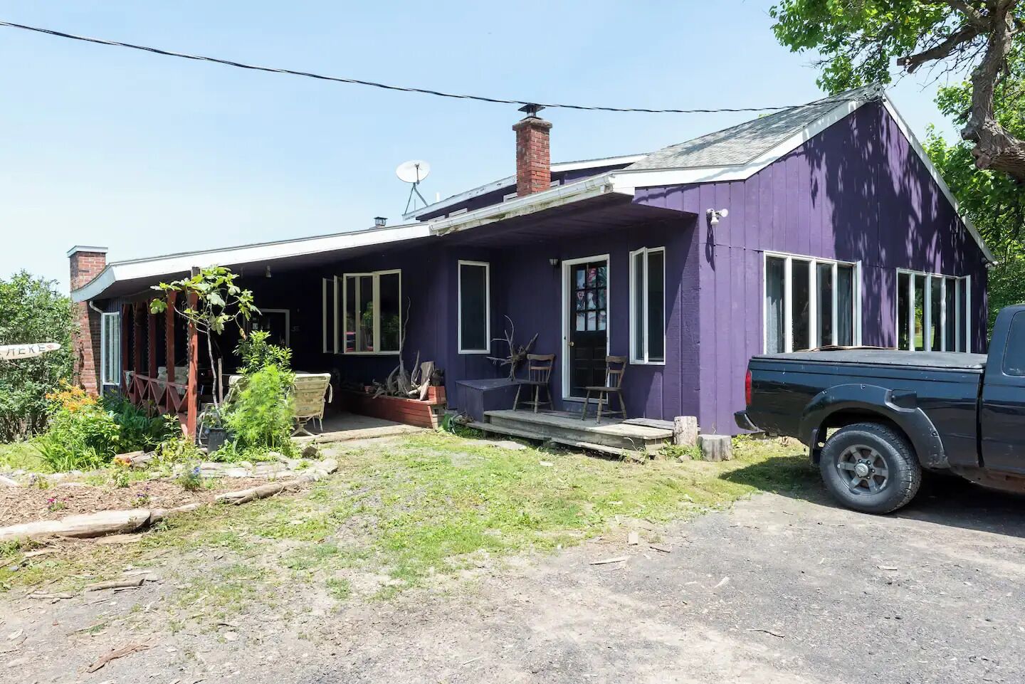 A single-story house with a purple exterior, a front porch, and a truck parked in front.