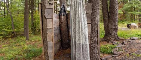 A rustic wooden structure with a metal door, a hanging bag, and a curtain.