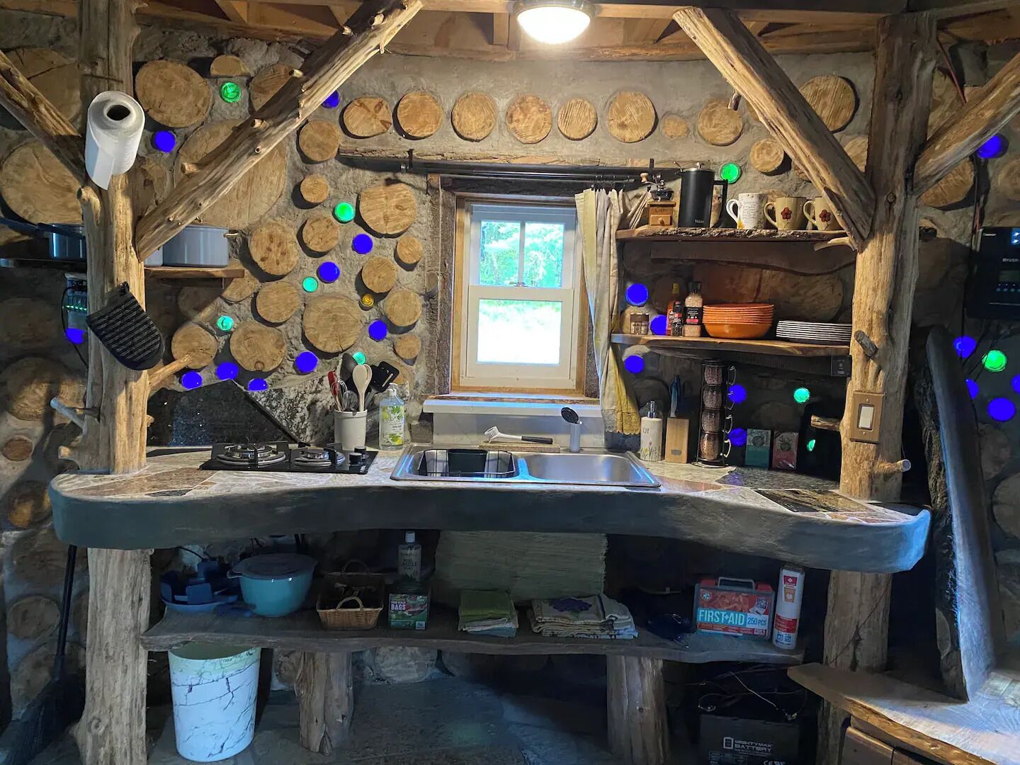 A rustic kitchen with a stone wall, wooden shelves, and a window.