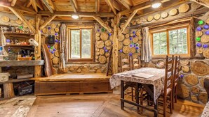 Ein rustikales Blockhaus-Interieur mit einer Holzbank, einem Esstisch mit Stühlen und einer Steinwand, die mit Holzscheiben verziert ist.