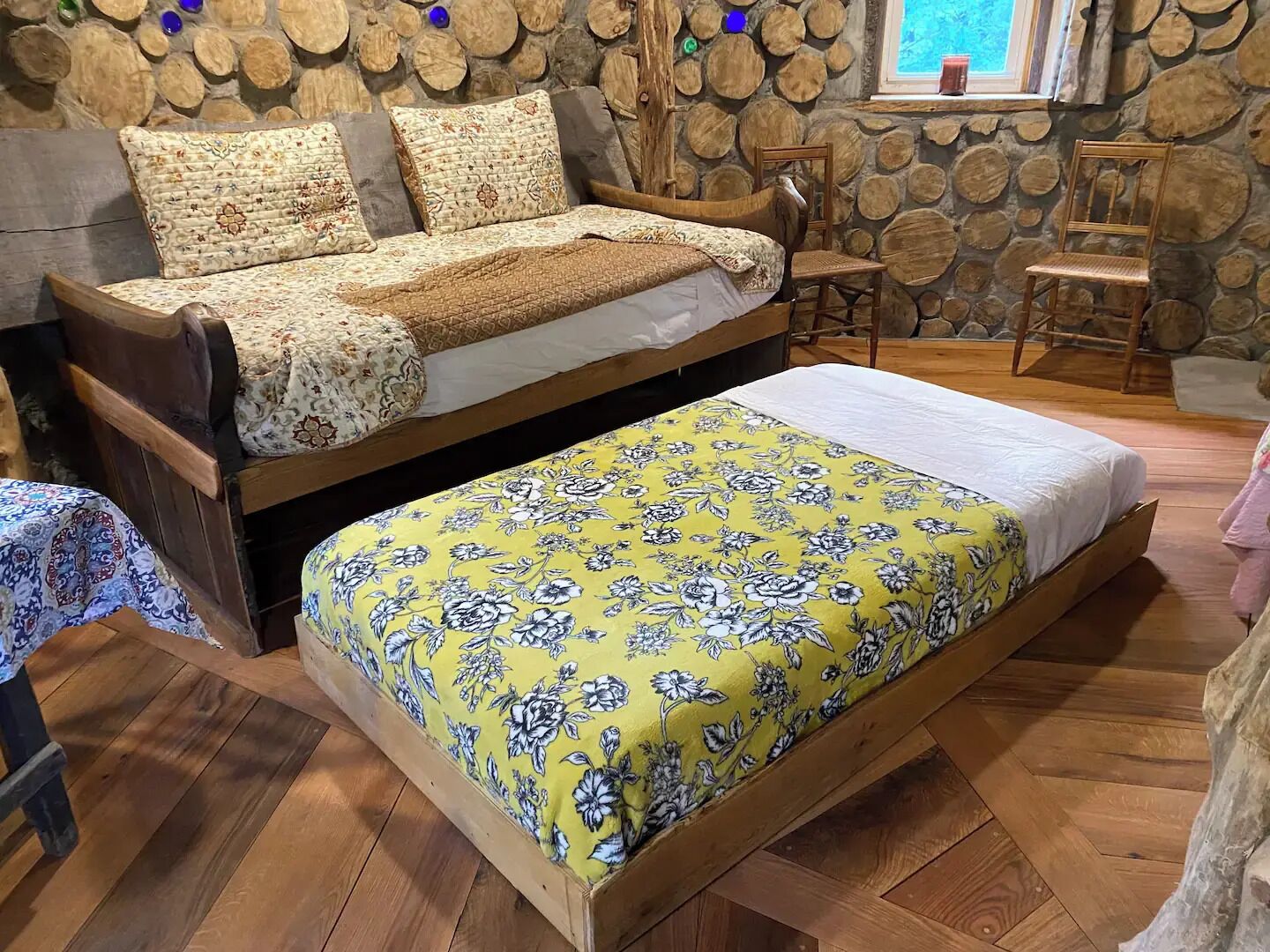A cozy bedroom with a wooden bed, a yellow floral bedspread, and a stone wall with logs.