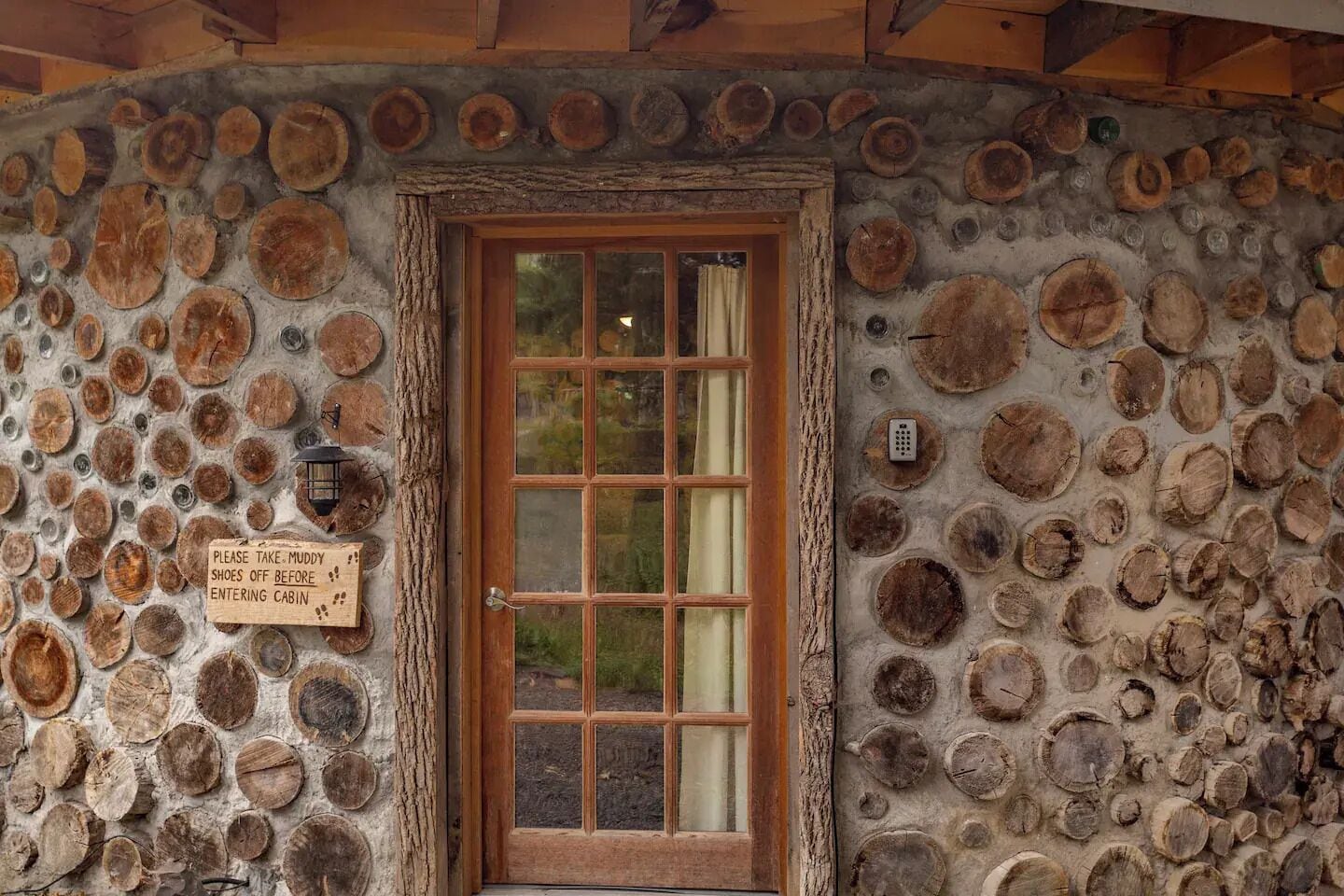 A cabin entrance with a wooden door and a sign instructing to remove shoes before entering.