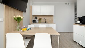 Eine moderne Küche mit weißen Schränken, einem Flachbildfernseher und einem Essbereich mit einem Holztisch und weißen Stühlen.