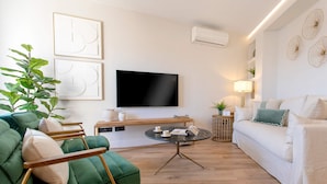 Un salon moderne avec un canapé vert, un canapé blanc, une table basse ronde et un téléviseur à écran plat fixé au mur.