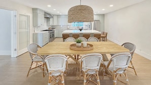 A modern kitchen with white cabinets, a central island, and a dining area with wicker chairs and a wooden table. - Ocean Front+ Theater Room +Hot Tub + Game Room (Carlsbad)