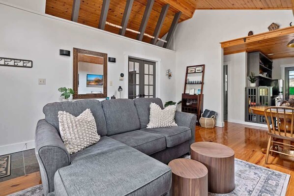 A modern living room with a grey sectional sofa, wooden coffee table, and a dining area with a wooden table and chairs.