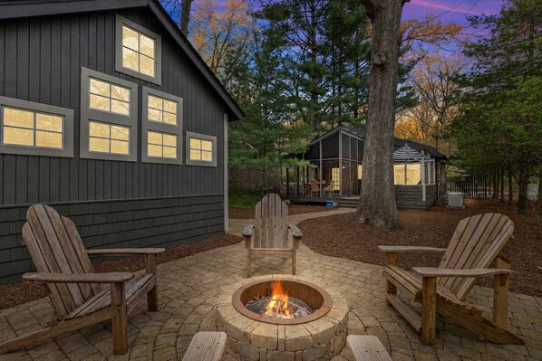 A house with a fire pit and Adirondack chairs in the backyard.