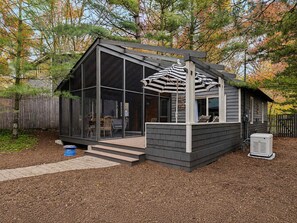 A modern house with a glass extension, a covered patio, and a wooden deck. - Juniper Presents Meadow Pines: Pet-Friendly Cottage w/ Hot Tub, Steps to Lake (Michigan City)