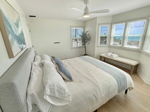 Une chambre à coucher comprenant un lit, un banc, un ventilateur de plafond et des fenêtres équipées de stores.