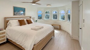 A spacious bedroom with a large bed, a ceiling fan, and a view of palm trees through arched windows. - Oceanfront- Views from balcony-Movie Room-Hot tub (Carlsbad)