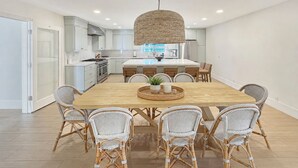 A modern kitchen with white cabinets, a central island, and a dining area with wicker chairs and a wooden table. - Oceanfront- Views from balcony-Movie Room-Hot tub (Carlsbad)