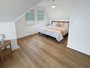 Ein Schlafzimmer mit einem Bett, einem Deckenventilator und zwei Fenstern mit Jalousien.