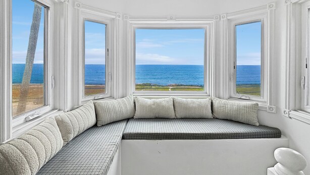 Een kamer met een gebogen bank, grote ramen en uitzicht op de oceaan.