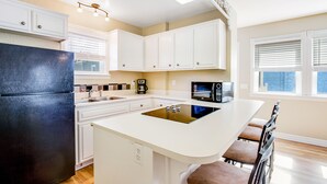 A modern kitchen with white cabinets, a black refrigerator, a microwave, and a large island with bar stools.