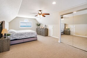Een slaapkamer met een bed, dressoir, spiegel, plafondventilator en een raam met jaloezieën.