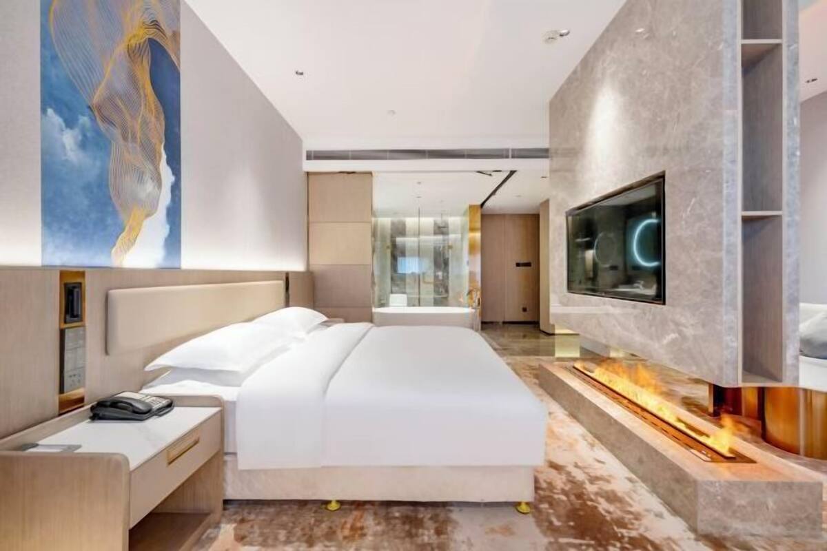 A modern hotel room with a large bed, a TV mounted on the wall, and a fireplace.