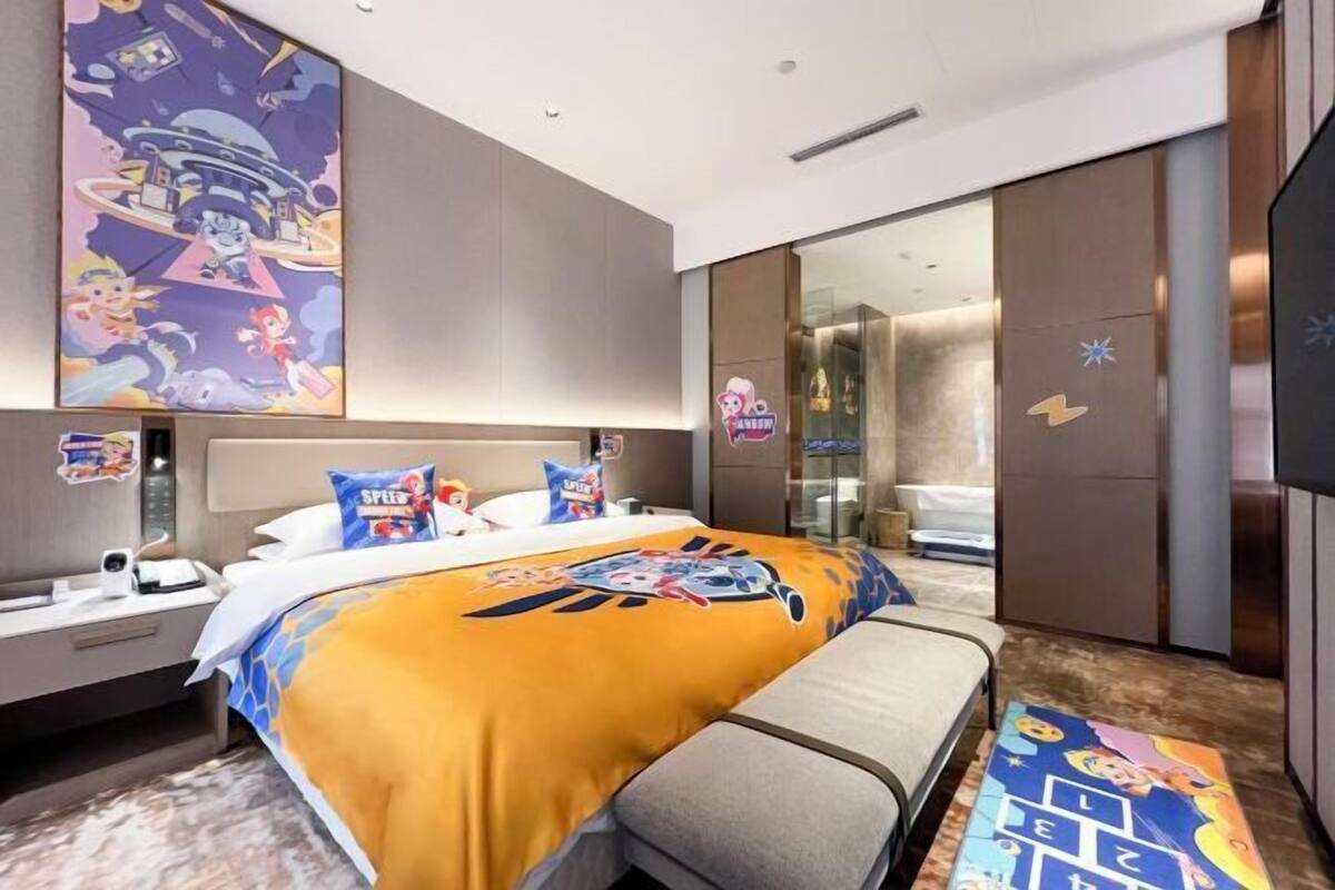 A modern hotel room with a large bed, a bedside table, a mirror, and a wardrobe.