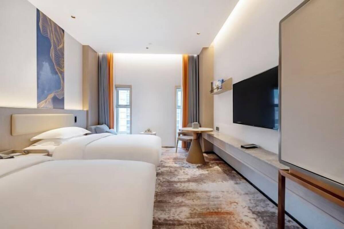 A hotel room with two beds, a TV, a small table, and a window.