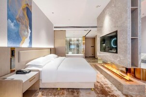 Una habitación de hotel moderna con una cama grande, un televisor montado en la pared y una chimenea.