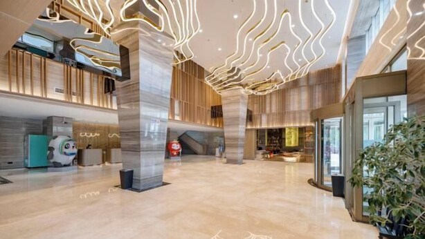 A spacious lobby with a high ceiling, modern lighting, and a central staircase.