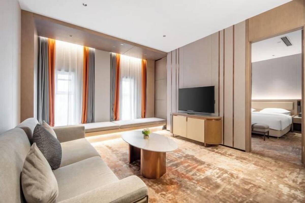 A modern hotel room with a sofa, a small round table, a TV, and a bed.