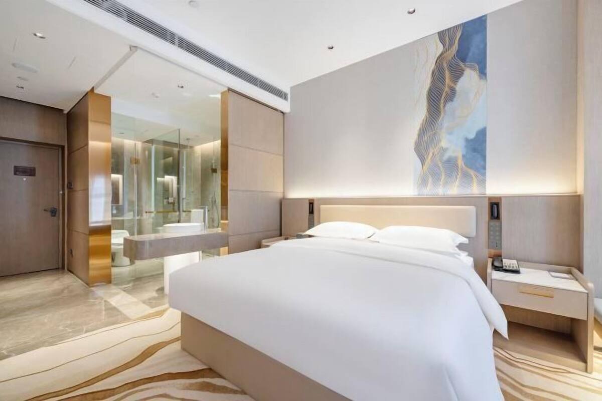 A modern hotel room with a large bed, a glass-enclosed bathroom, and a contemporary wall art piece.