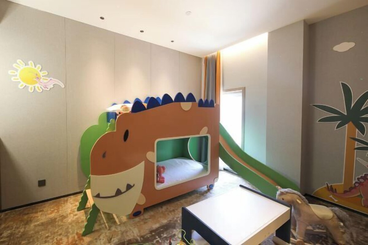 Espaço infantil com uma cama em formato de dinossauro e uma pequena escrivaninha.