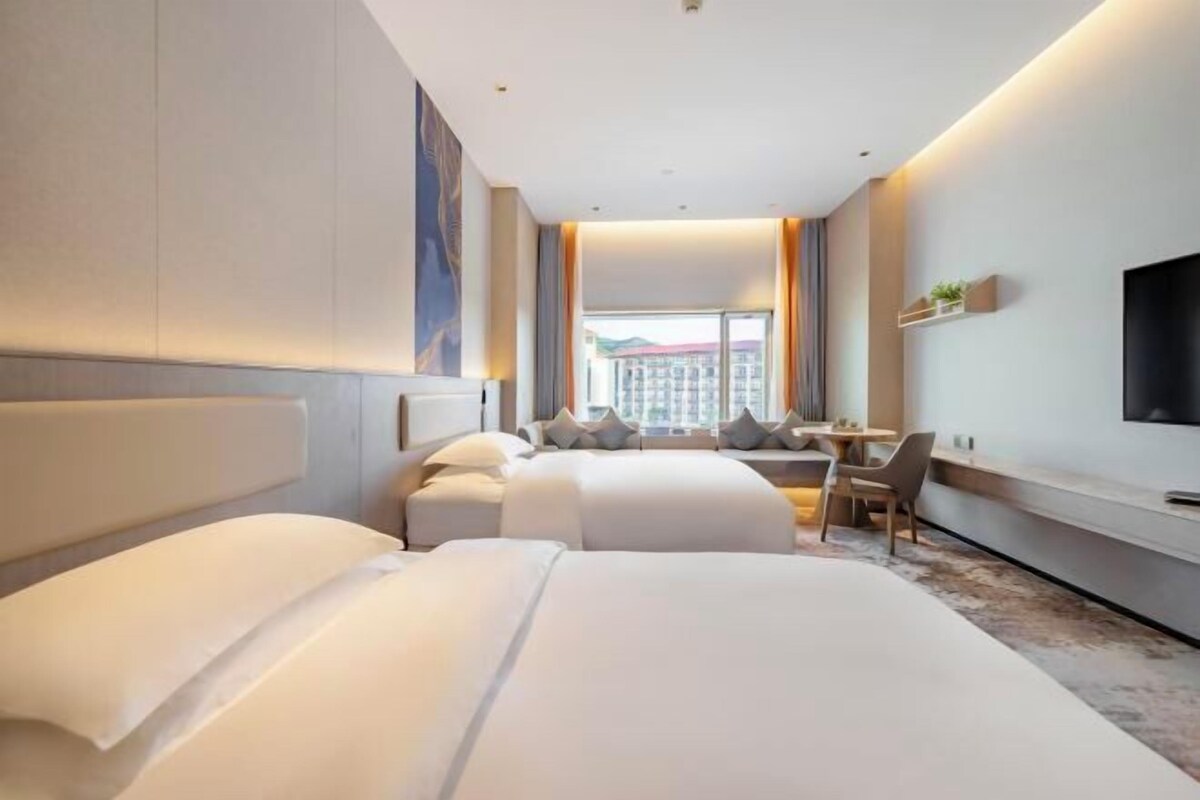 Quarto de hotel moderno com duas camas, uma escrivaninha e uma televisão.