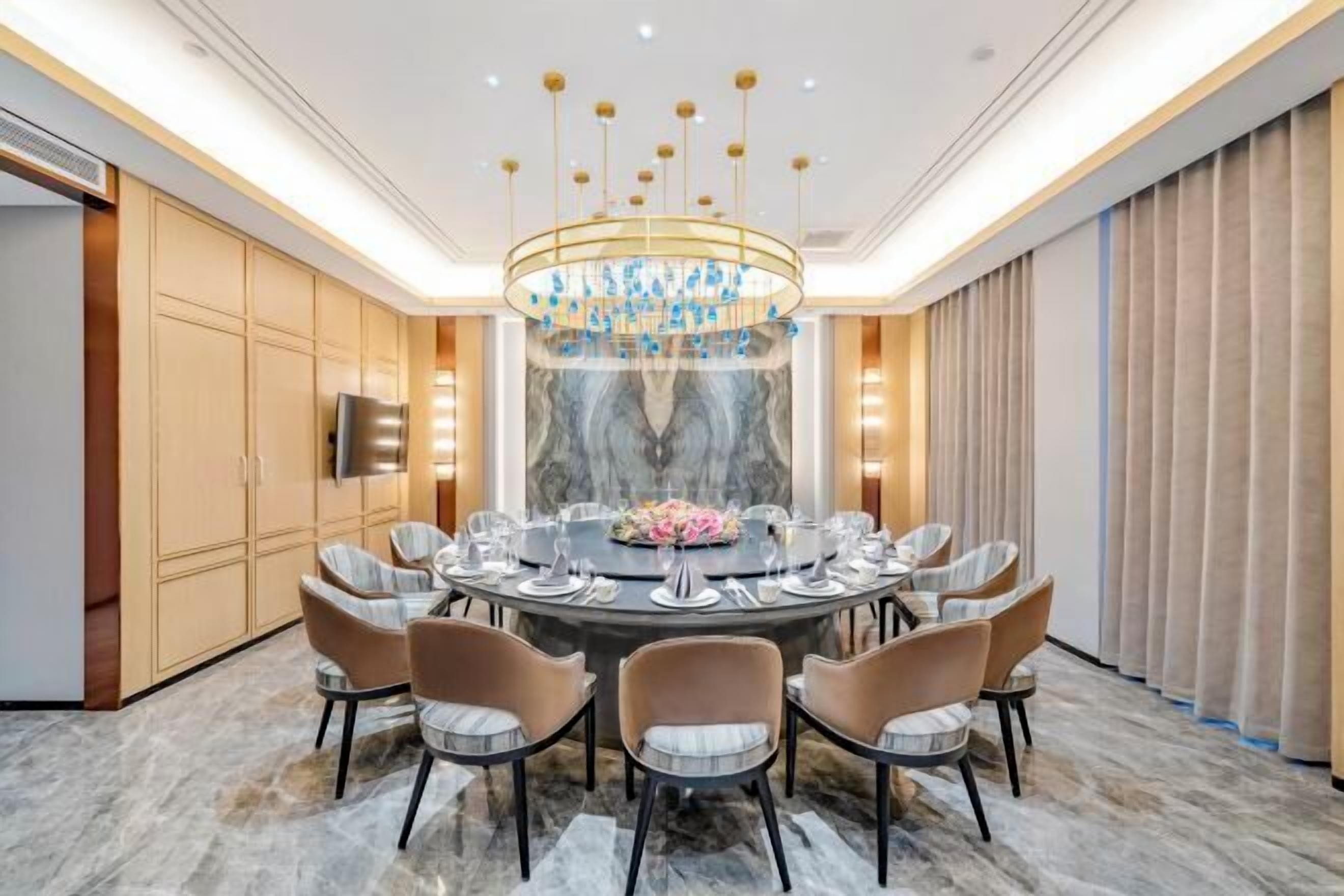 A modern dining area with a round table, eight chairs, and a central chandelier.